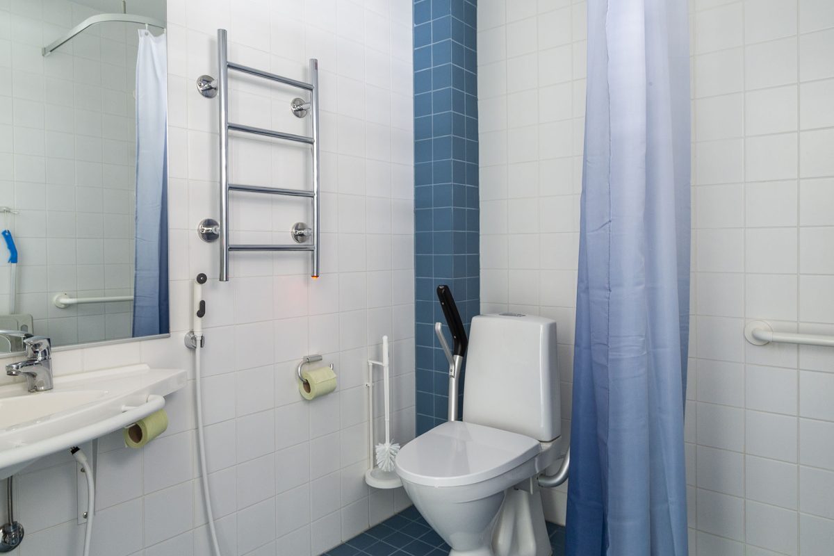 Badrum med räcken för rörelsehindrade vid handfat, dusch och toalett.