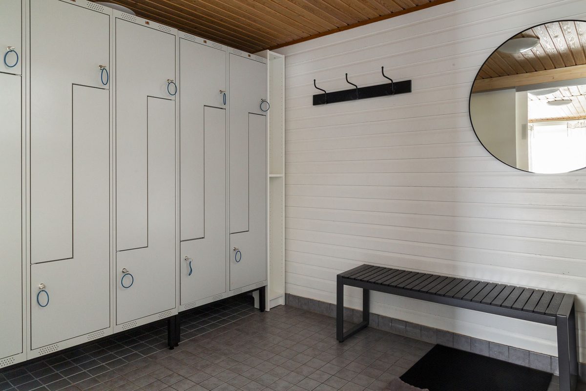 Sauna changing room with lockable cabinets, a bench, a mirror and a coat rack.