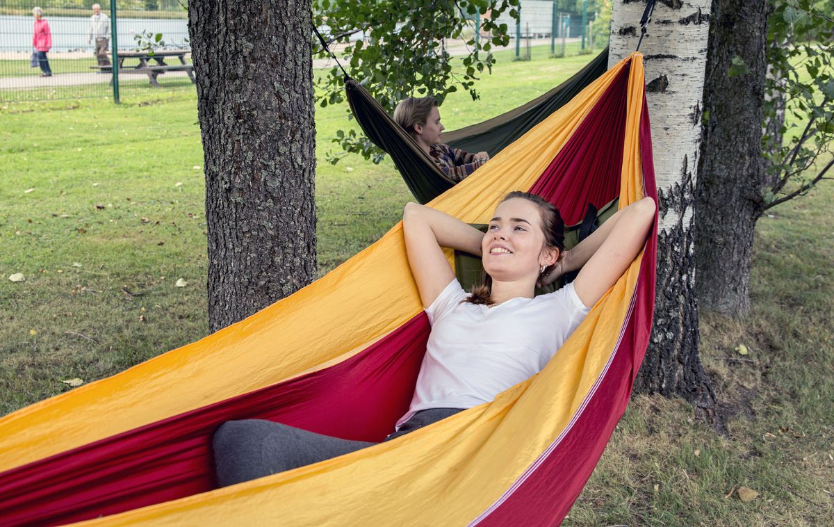 Two young people lounging on hammocks in the shade of trees.